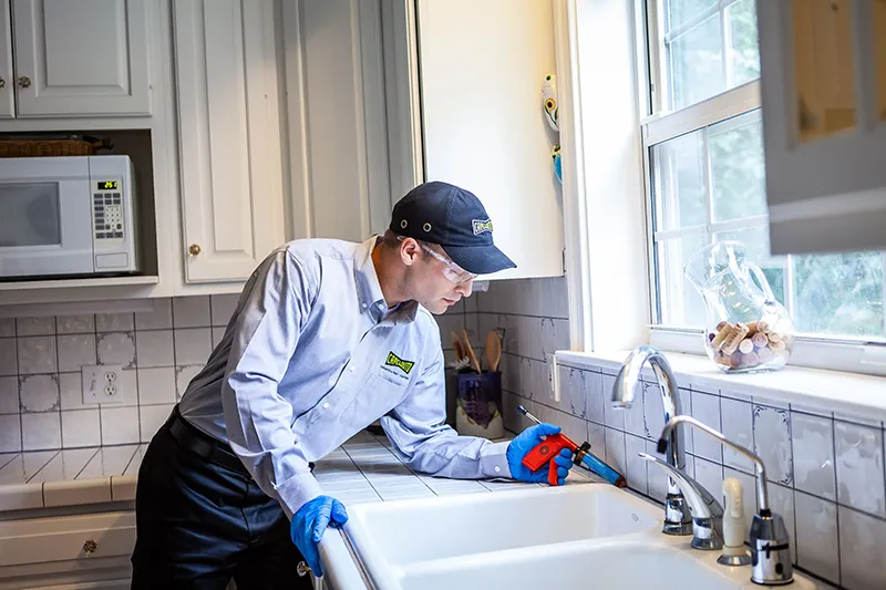 Pest control technician applying pest control treatment to a kitchen sink - Keep pests away from your kitchen with Capelouto Termite & Pest Control in Tallahassee, FL